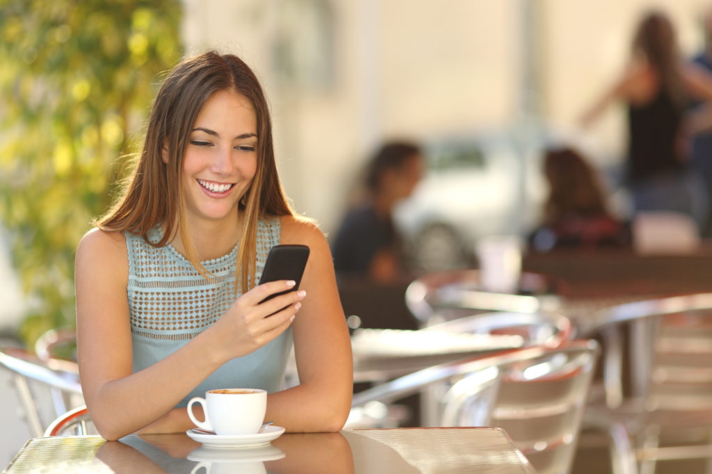 Girl texting on the smart phone in a restaurant terrace with an unfocused background / AntonioGiullemF