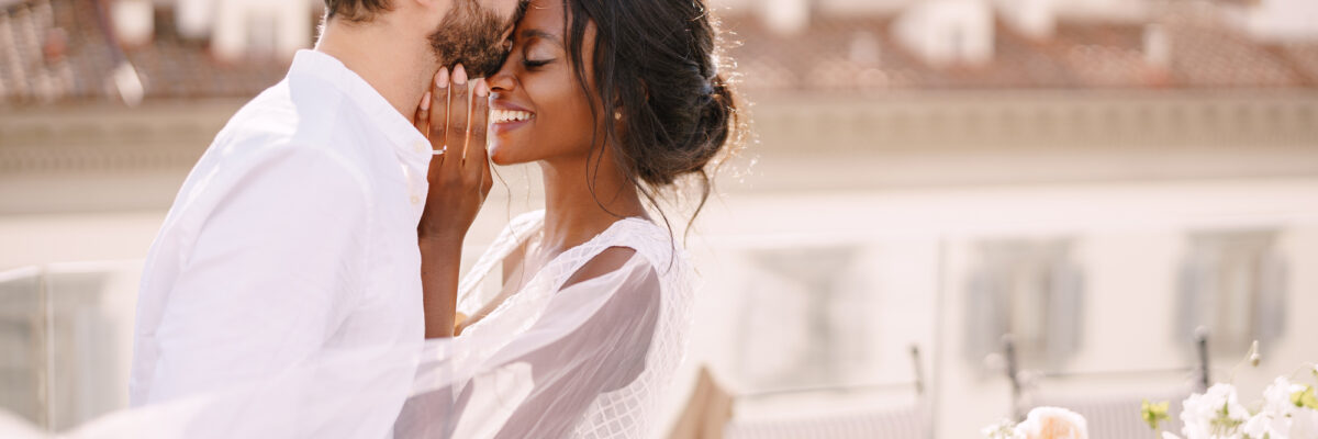 Destination wedding in Florence, Italy. Caucasian groom and African-American bride cuddle on the roof, in the sunny sunset light.