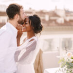 Destination wedding in Florence, Italy. Caucasian groom and African-American bride cuddle on the roof, in the sunny sunset light.