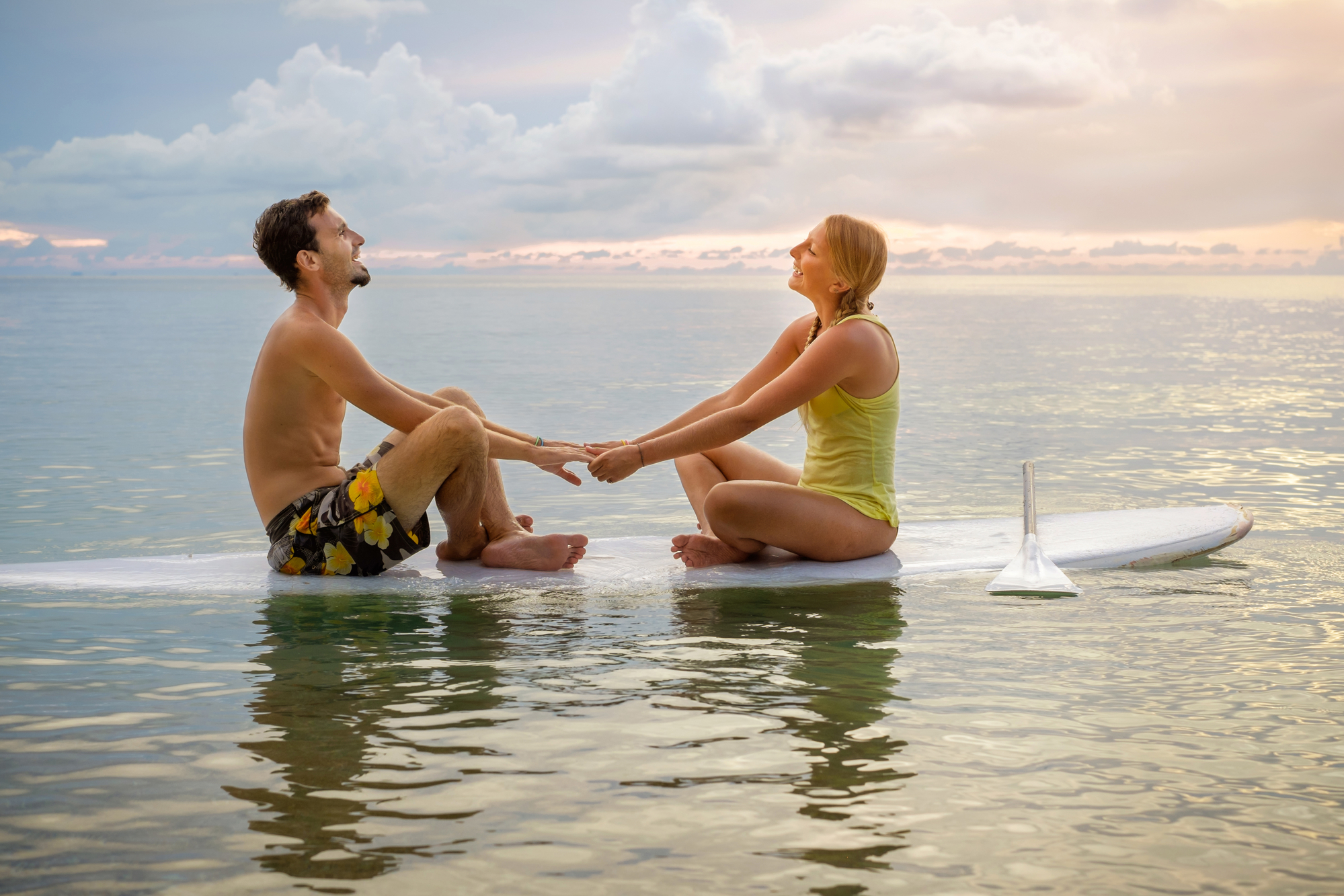 Young couple sitting on the paddle board near the beach and enjoying sunset / @Gilitukha - Deposit Photos