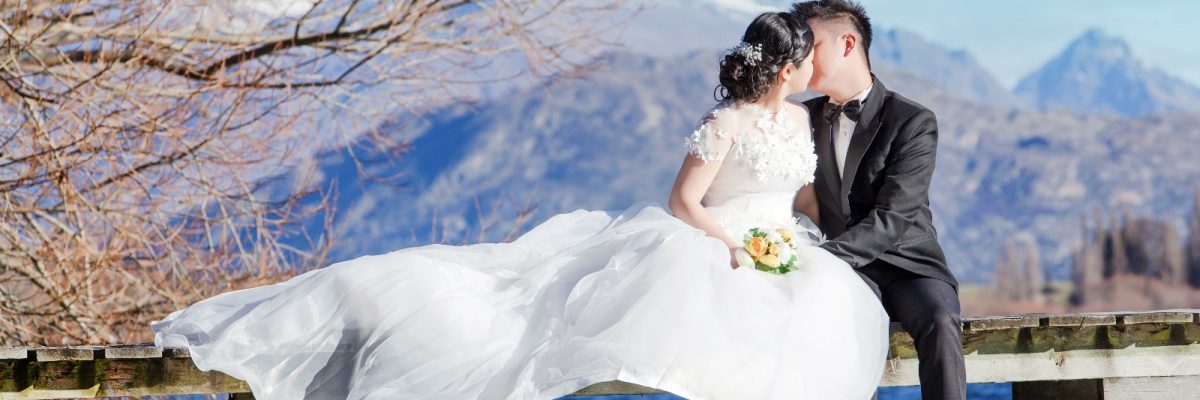 Bride and groom kissing on bridge by lake