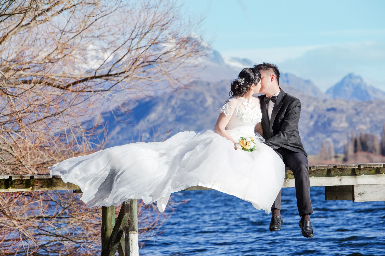 Bride and groom kissing on bridge by lake