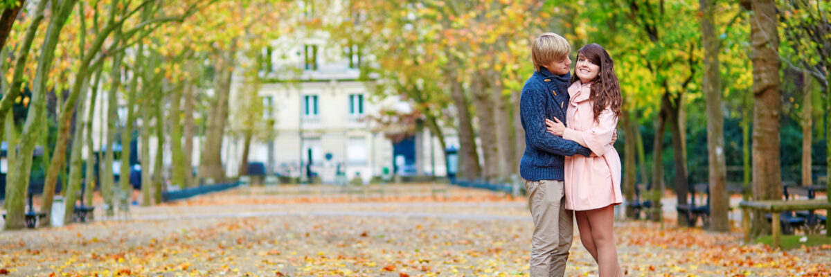 Romantic couple standing on driveway to a castle, about to kiss. The ground is covered in autumn leaves.