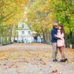 Romantic couple standing on driveway to a castle, about to kiss. The ground is covered in autumn leaves.